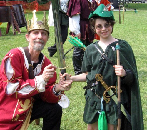 King Richard kneels to the left of young Robin Hood, gripping the sword